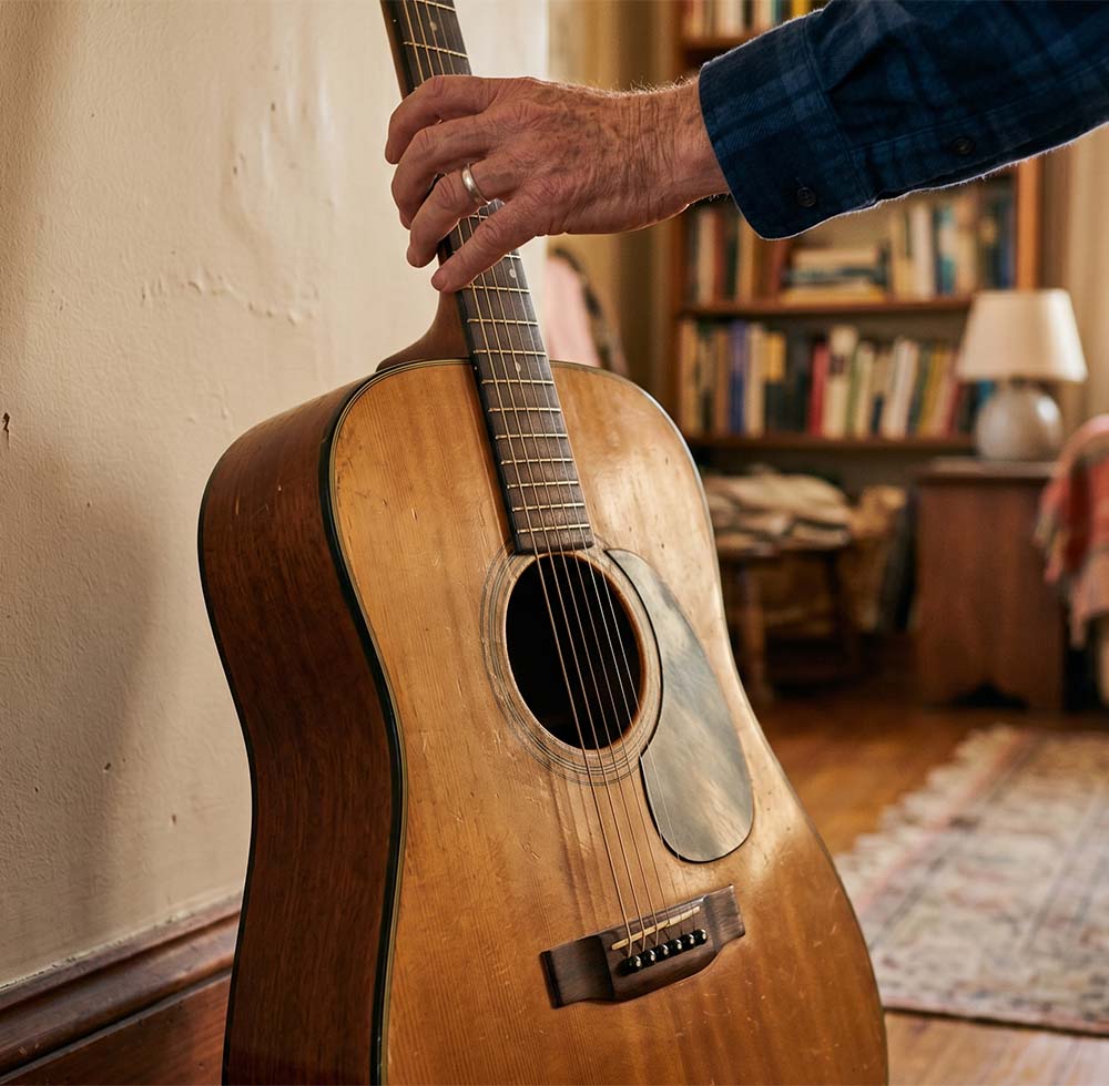 Adult hand reaching toward an acoustic guitar, suggesting a possible self still connected to music